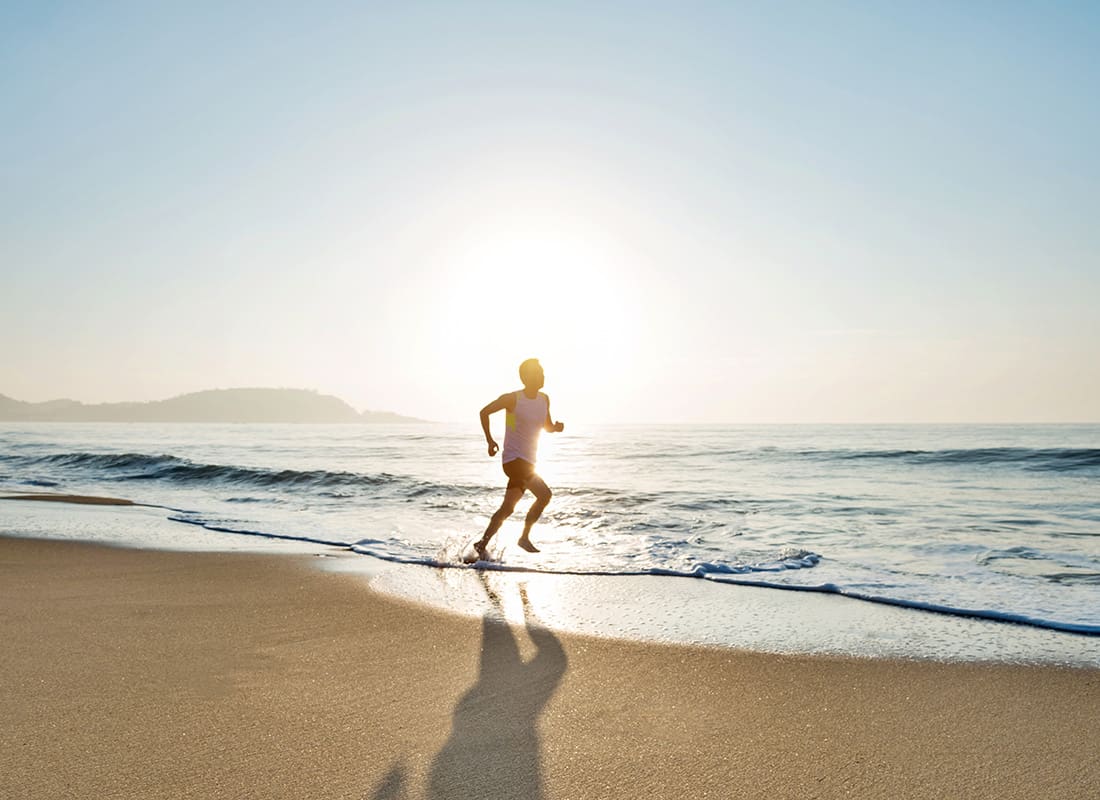 Insurance Solutions - View of a Man Jogging Along the Water on the Beach on a Sunny Day